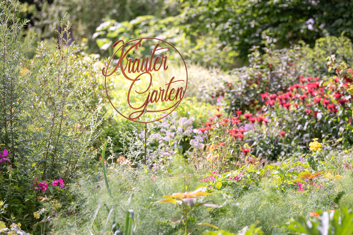 Rostiges Schild "Kräutergarten" inmitten von blühenden Stauden